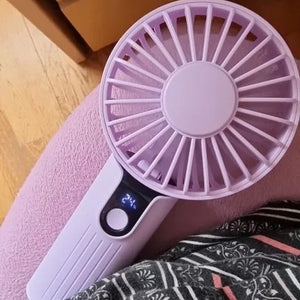 Ventilateur portable rose posé sur un tissu à motifs