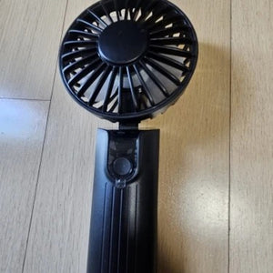 Ventilateur portable noir debout sur un parquet en bois