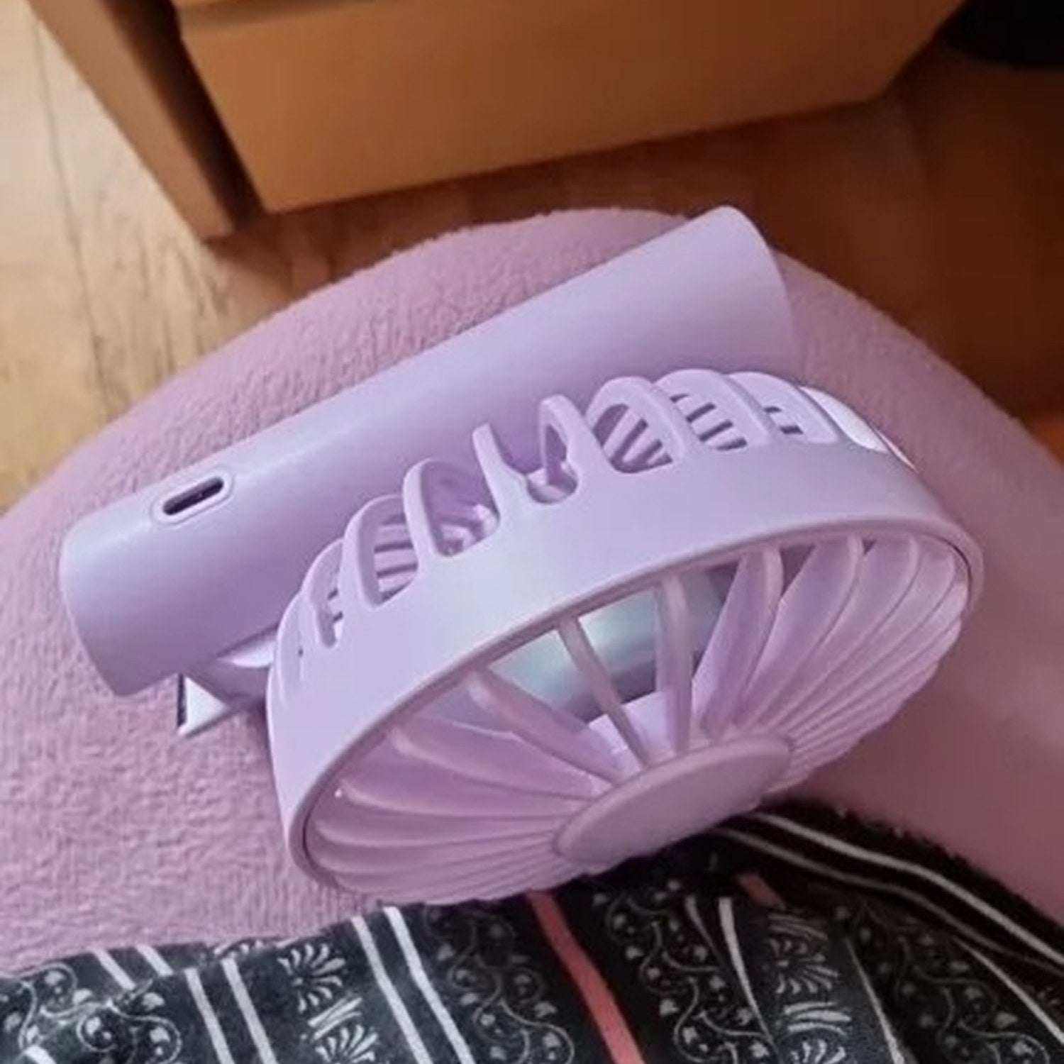 Ventilateur portable rose plié posé sur un tissu à motifs