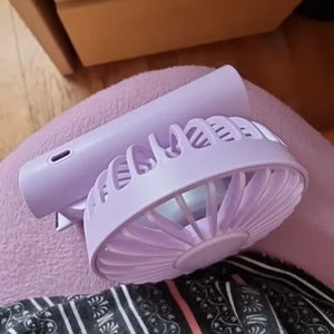 Ventilateur portable rose plié posé sur un tissu à motifs