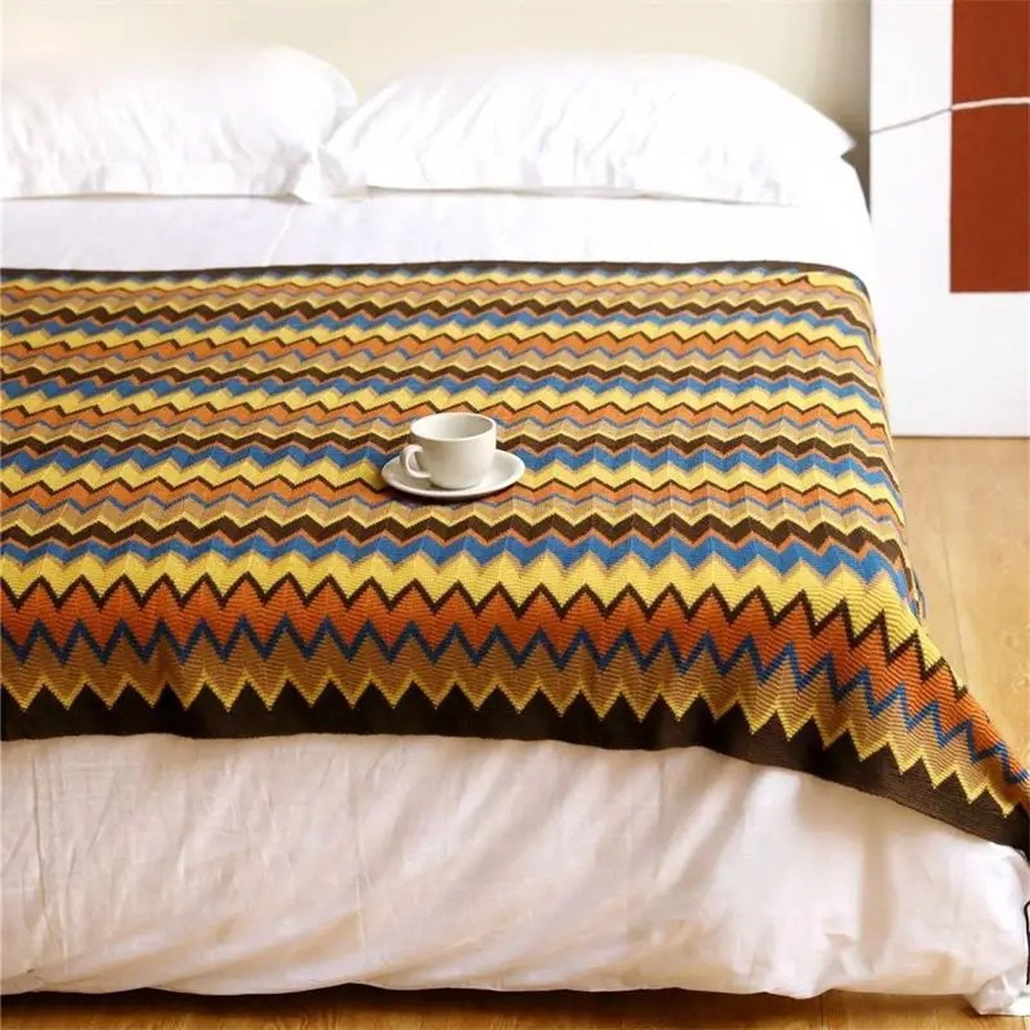 Plaid coloris doré tricoté chevrons posé à plat sur un lit avec tasse