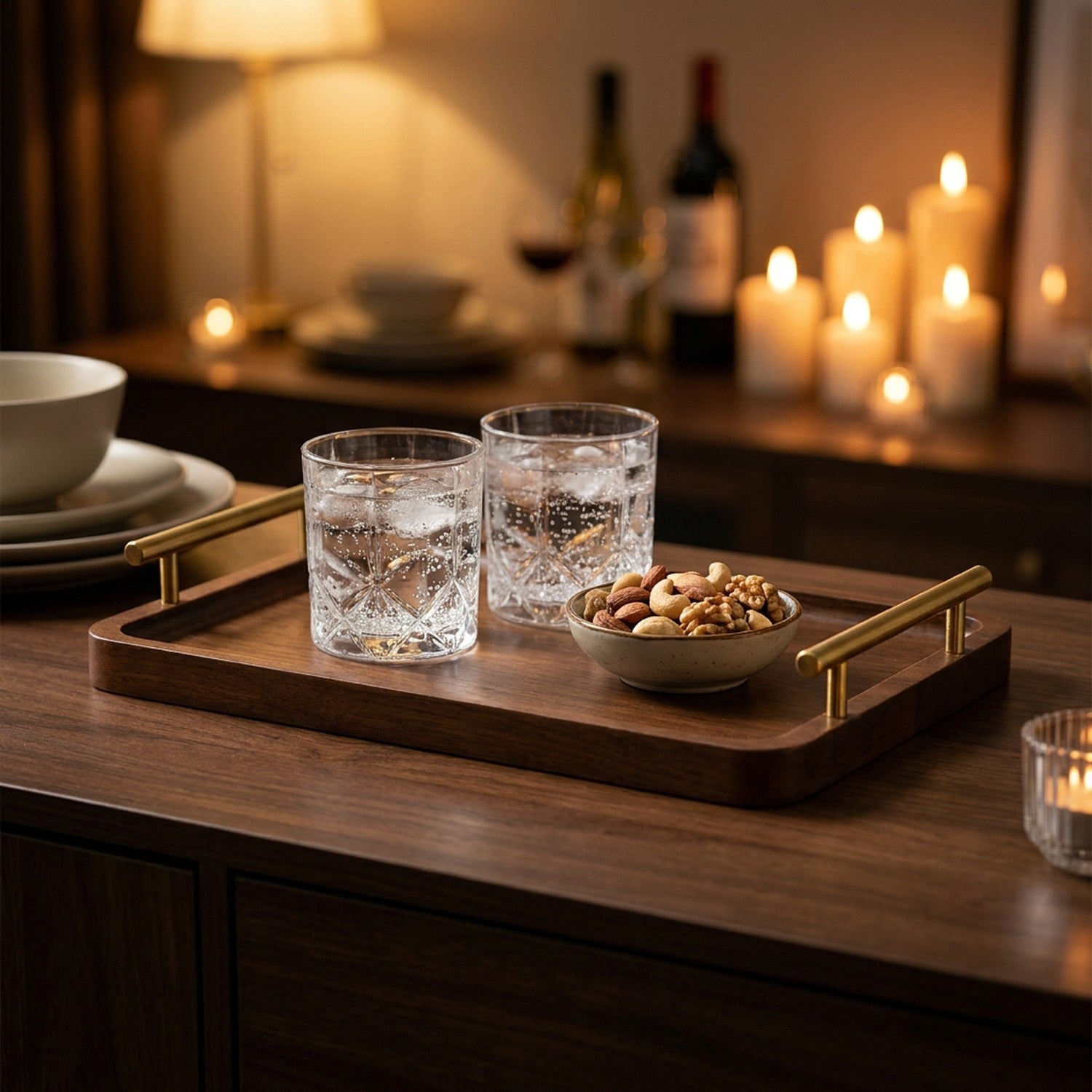 Plateau en bois à poignées dorées servant deux verres et un bol de noix à la lueur des bougies