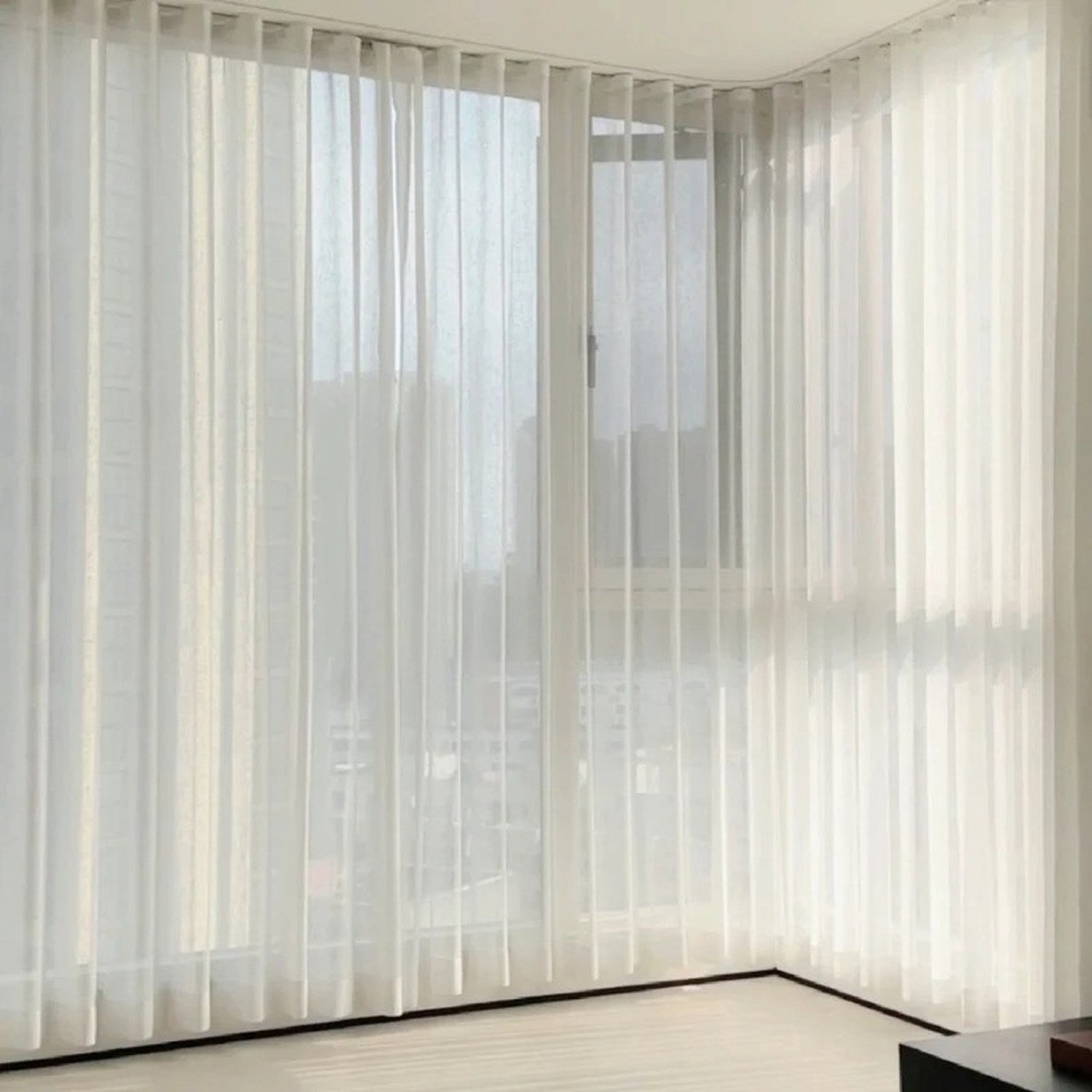 Rideau voile blanc effet vague habillant un angle de fenêtre dans un salon lumineux