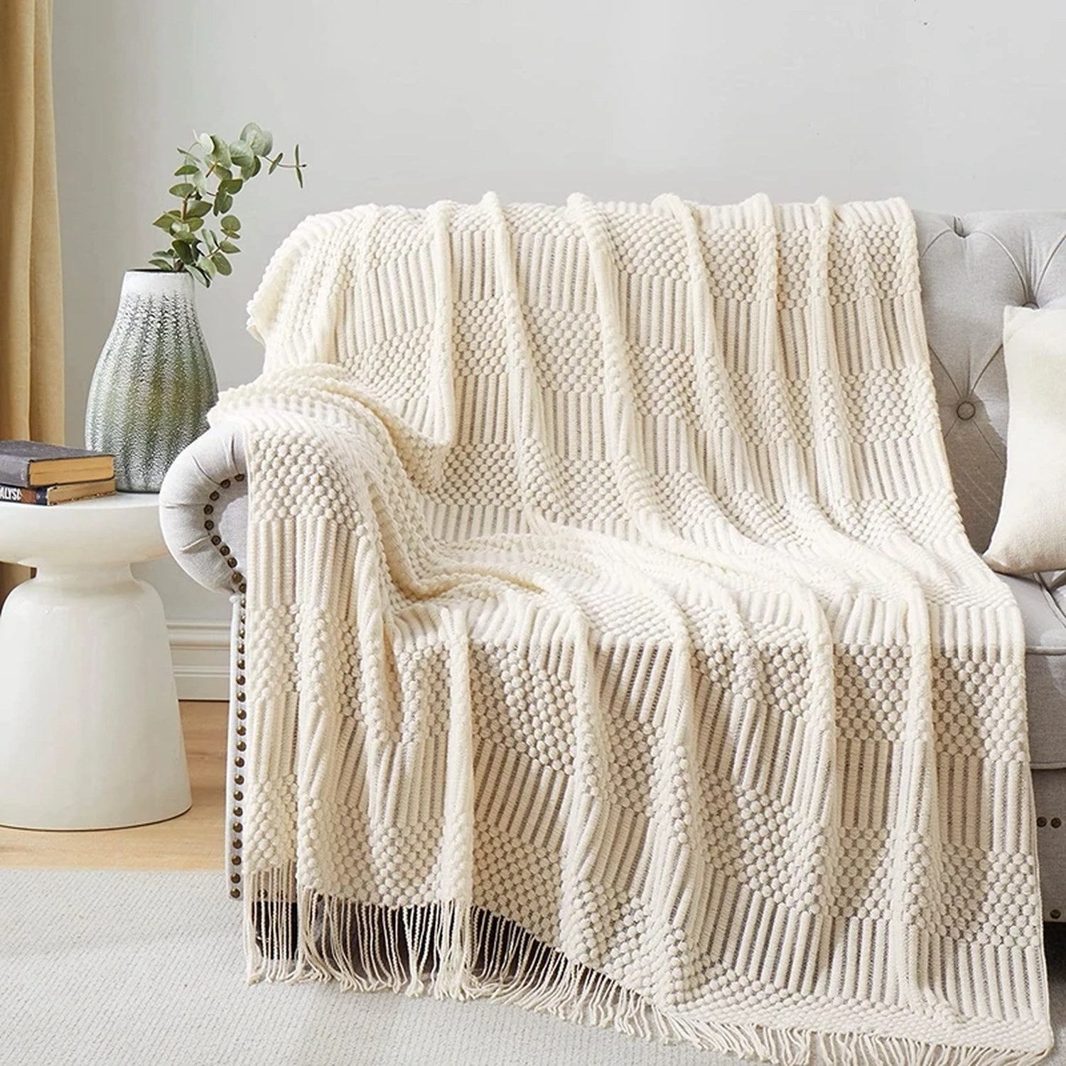 Plaid tricoté crème drapé sur un canapé gris avec branche d eucalyptus