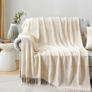 Plaid tricoté crème drapé sur un canapé gris avec branche d eucalyptus