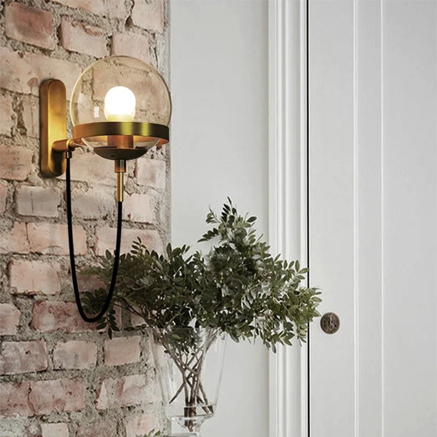 Applique murale boule de verre dorée fixée sur un mur de brique près d'une plante verte