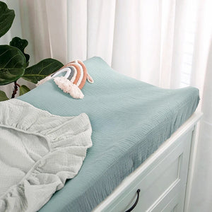 Housse de matelas à langer sauge unie près d'une fenêtre avec plante verte