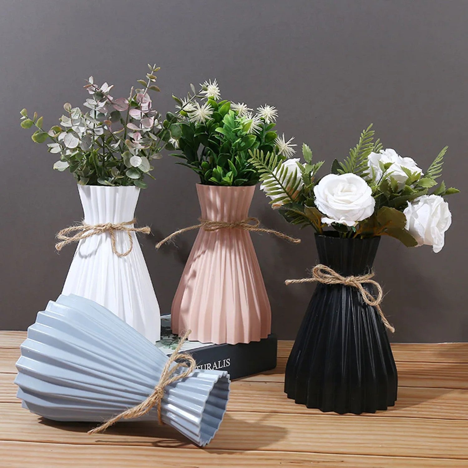 Quatre vases origami plissés de différentes couleurs avec des plantes vertes