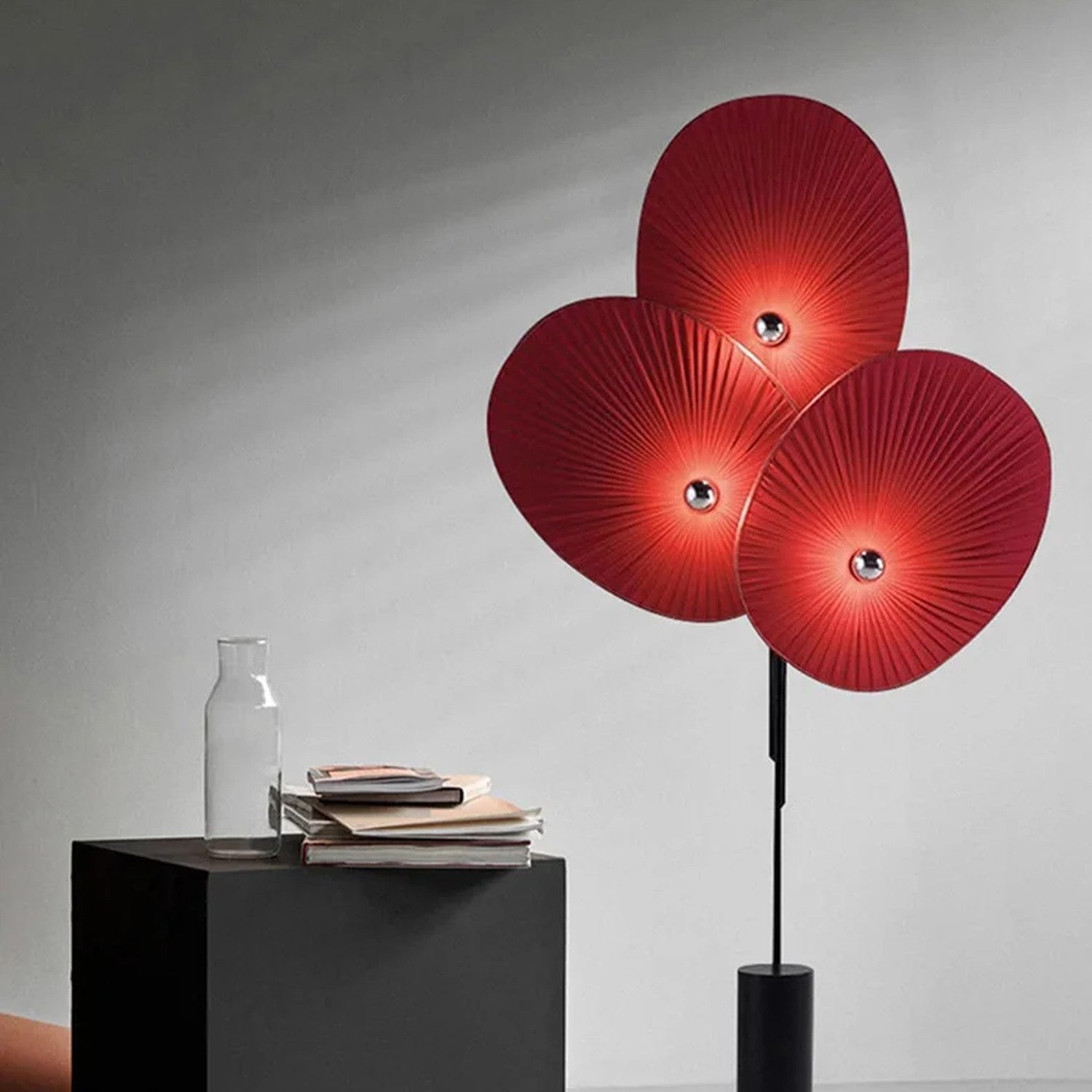 Lampadaire design 3 pétales rouge allumé sur fond neutre gris