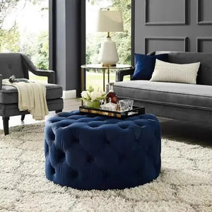 Tabouret pouf bleu marine en velours utilisé comme table basse dans un salon