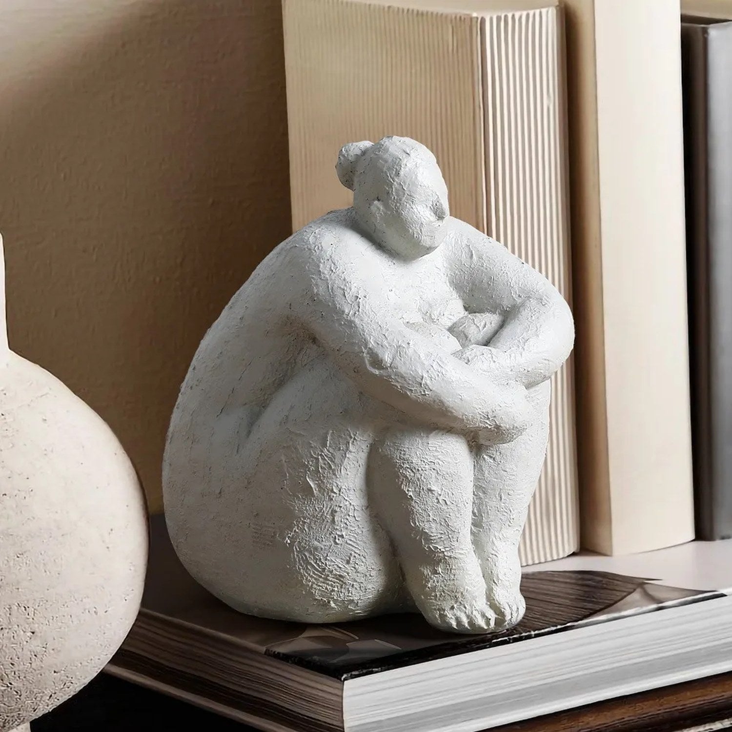 Figurine femme ronde blanche assise sur étagère avec livres et vase