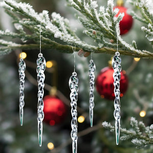 Glaçons transparents torsadés avec attaches suspendus à une branche de sapin enneigée avec boules rouges