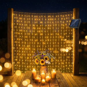 Guirlande rideau LED solaire lumière chaude suspendue entre poteaux bois en jardin la nuit avec tournesols et bougies