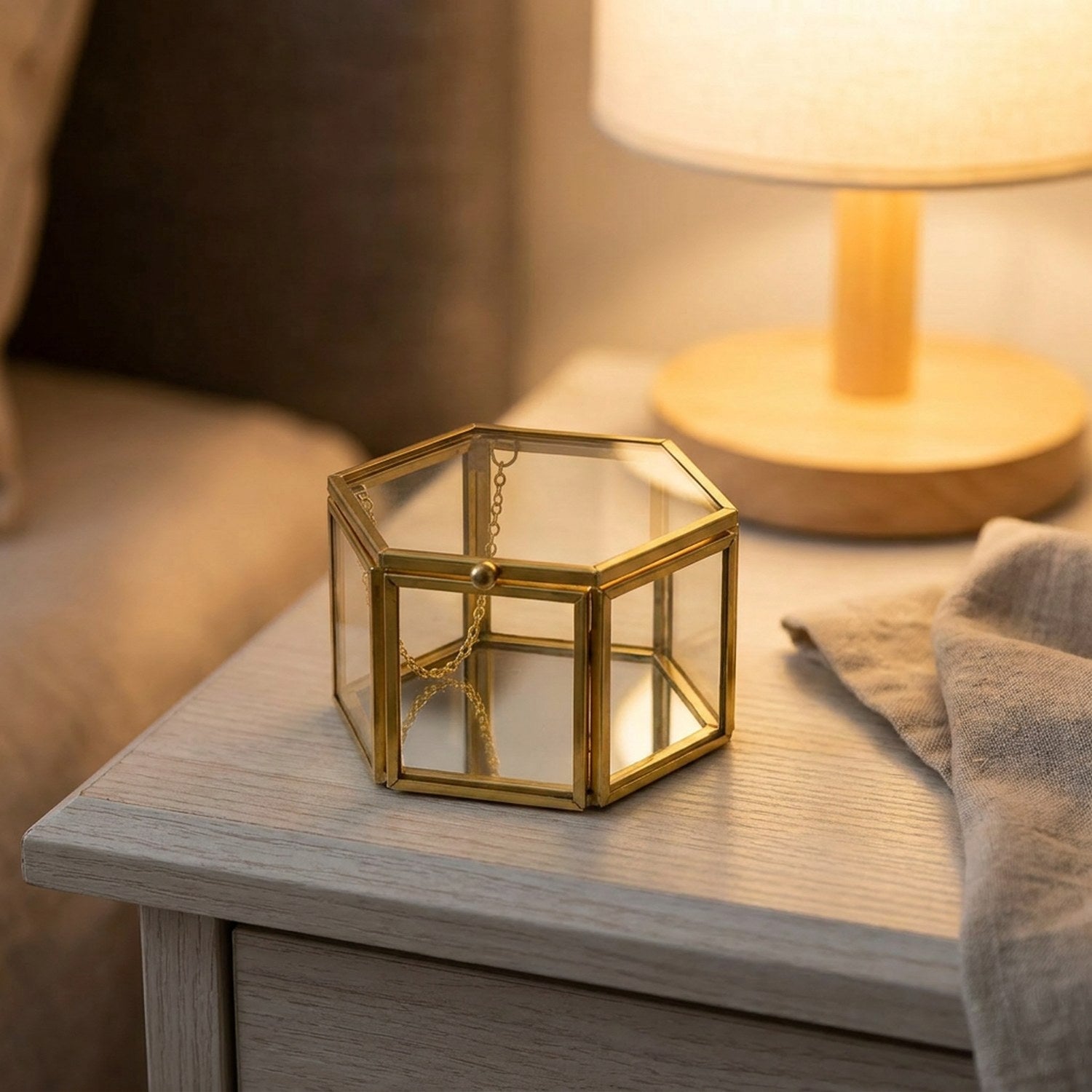 Boîte à bijoux hexagonale en verre fermée sur une table de nuit avec une lampe chaleureuse