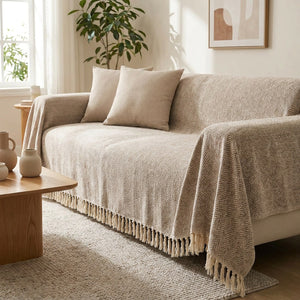 Housse de canapé en chenille beige à franges drapée sur un canapé dans un salon lumineux