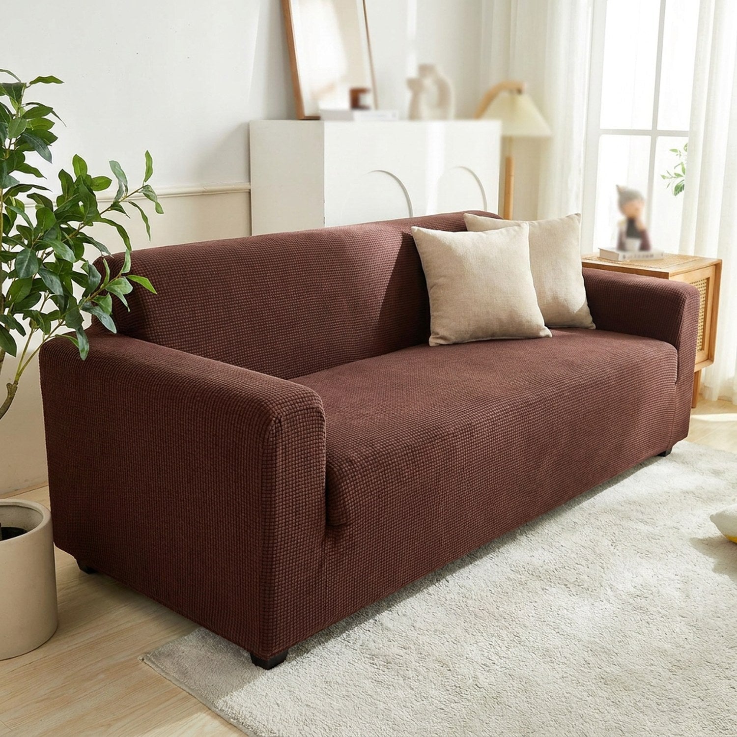 Housse de canapé extensible en jacquard marron installée sur un canapé dans un salon chaleureux