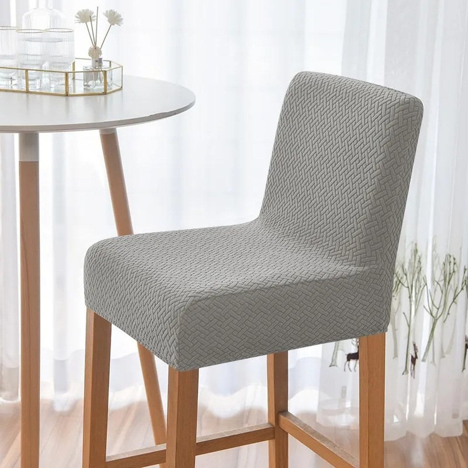 Tabouret de bar habillé d'une housse grise près d'une table d'appoint et d'un rideau voilage