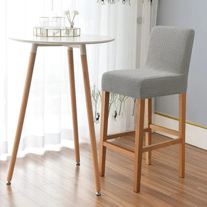 Chaise haute avec housse grise posée à côté d'une table de bar ronde en bois