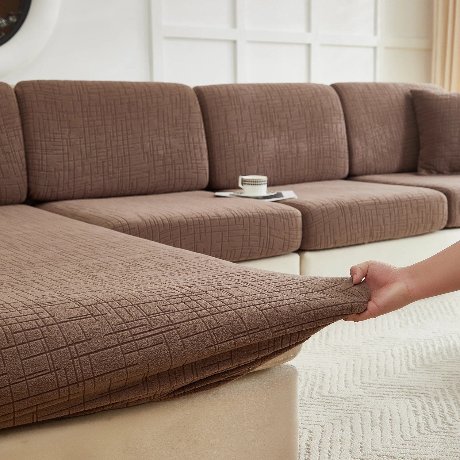Détail d'une housse de coussin marron étirée à la main pour montrer l'élasticité