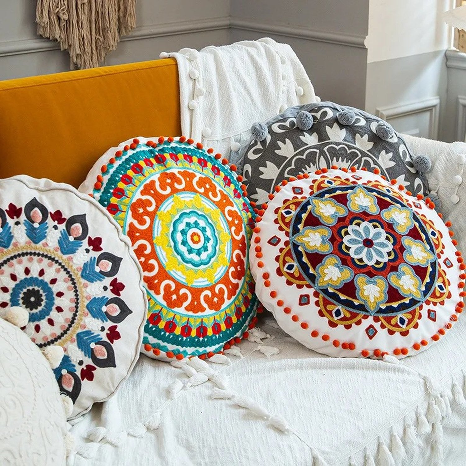 Quatre housses de coussin rondes brodées mandala aux couleurs et motifs bohèmes différents sur un canapé