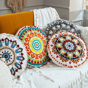 Quatre housses de coussin rondes brodées mandala aux couleurs et motifs bohèmes différents sur un canapé