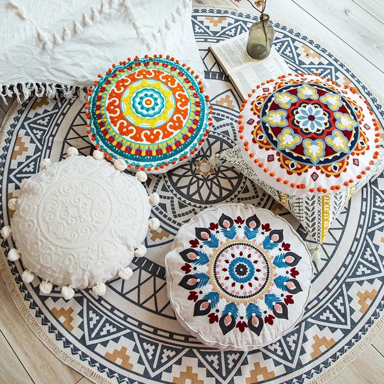 Housses de coussin mandala colorées posées sur un tapis bohème avec un livre et un vase