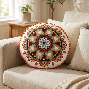 Housse de coussin ronde brodée mandala rouge et doré posée sur un canapé en lin beige