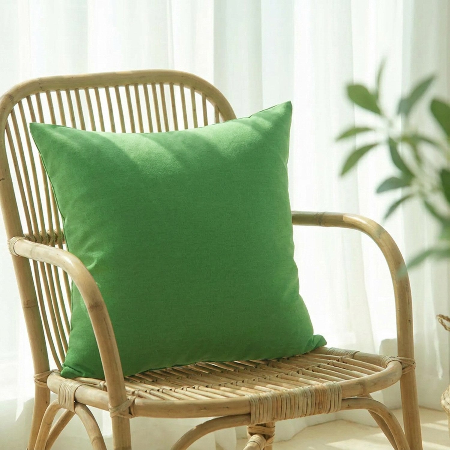 Housse de coussin vert uni sur un fauteuil en rotin