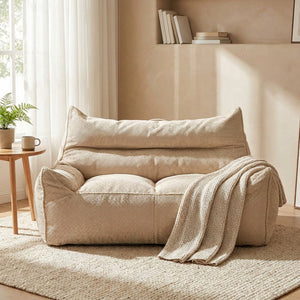 Housse de pouf poire beige installée dans un salon lumineux avec plaid et plante
