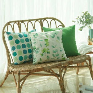 Trois housses de coussin vertes motifs feuillage pois et uni alignées sur un banc en rotin