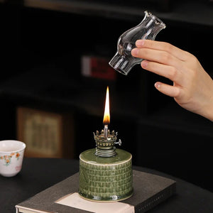 Lampe à pétrole en céramique céladon, main posant le verre protecteur allumé