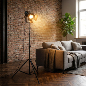 Lampadaire trépied projecteur noir dans un salon industriel avec canapé gris