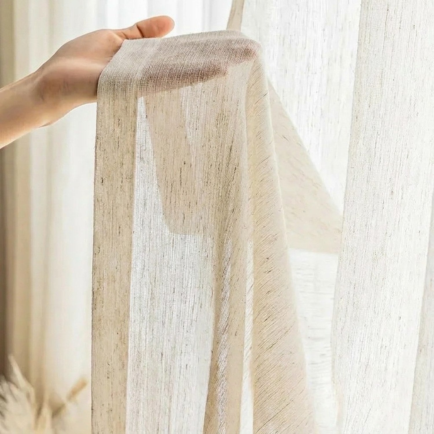 Détail du tissu tulle effet lin tenu à la main devant une fenêtre