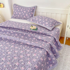 Couvre-lit matelassé violet à fleurs roses posé sur un lit avec taies assorties