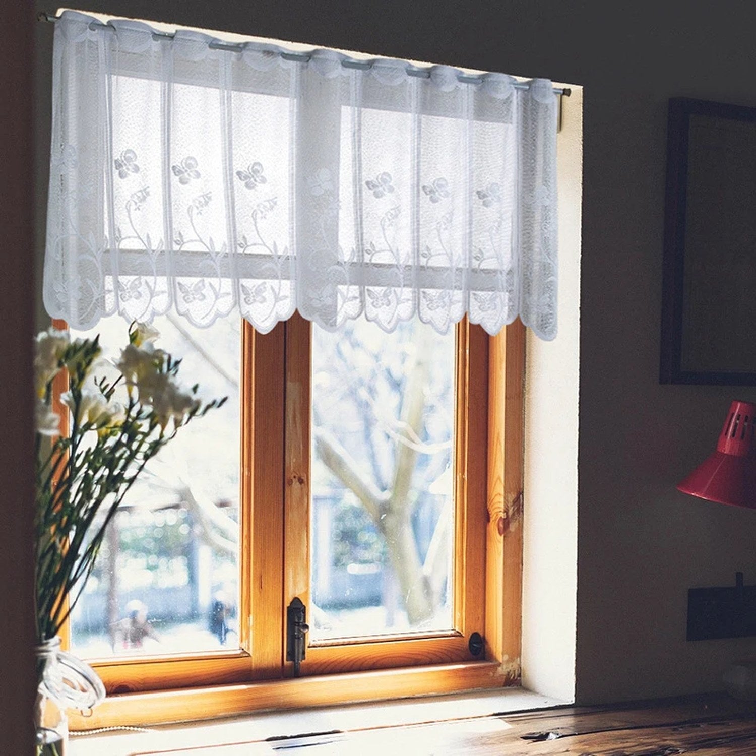 Voilage en dentelle blanche installé sur une fenêtre en bois avec fleurs blanches