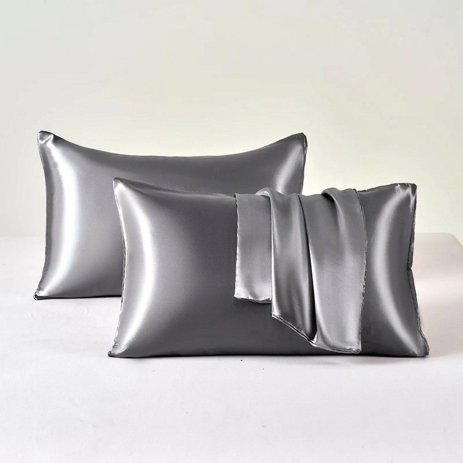 Deux taies d'oreiller en satin gris posées sur un fond clair