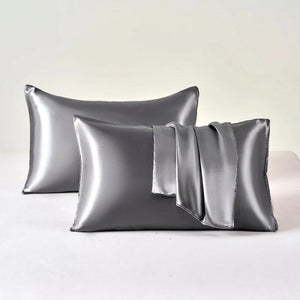 Deux taies d'oreiller en satin gris posées sur un fond clair