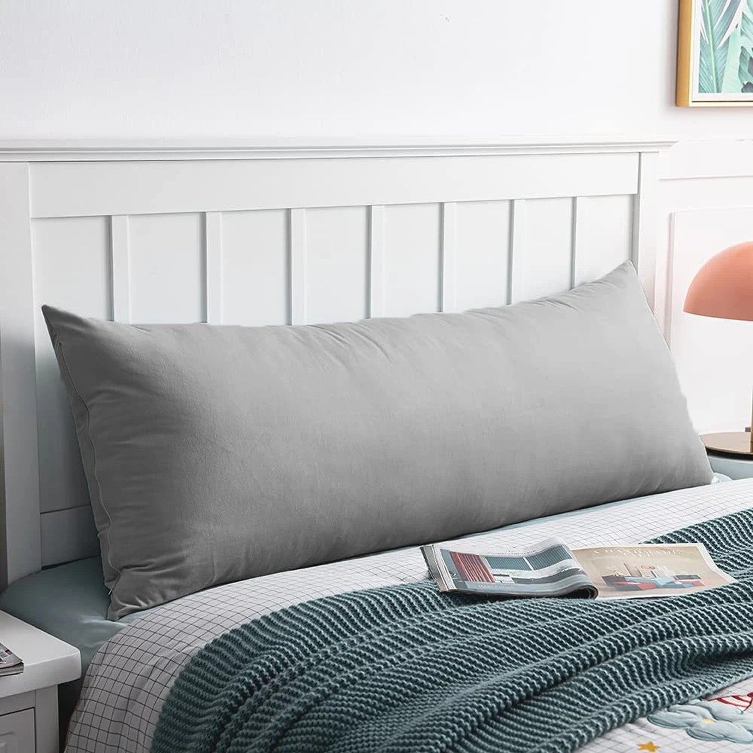 Housse de coussin en velours gris posée sur un lit contre une tete de lit blanche
