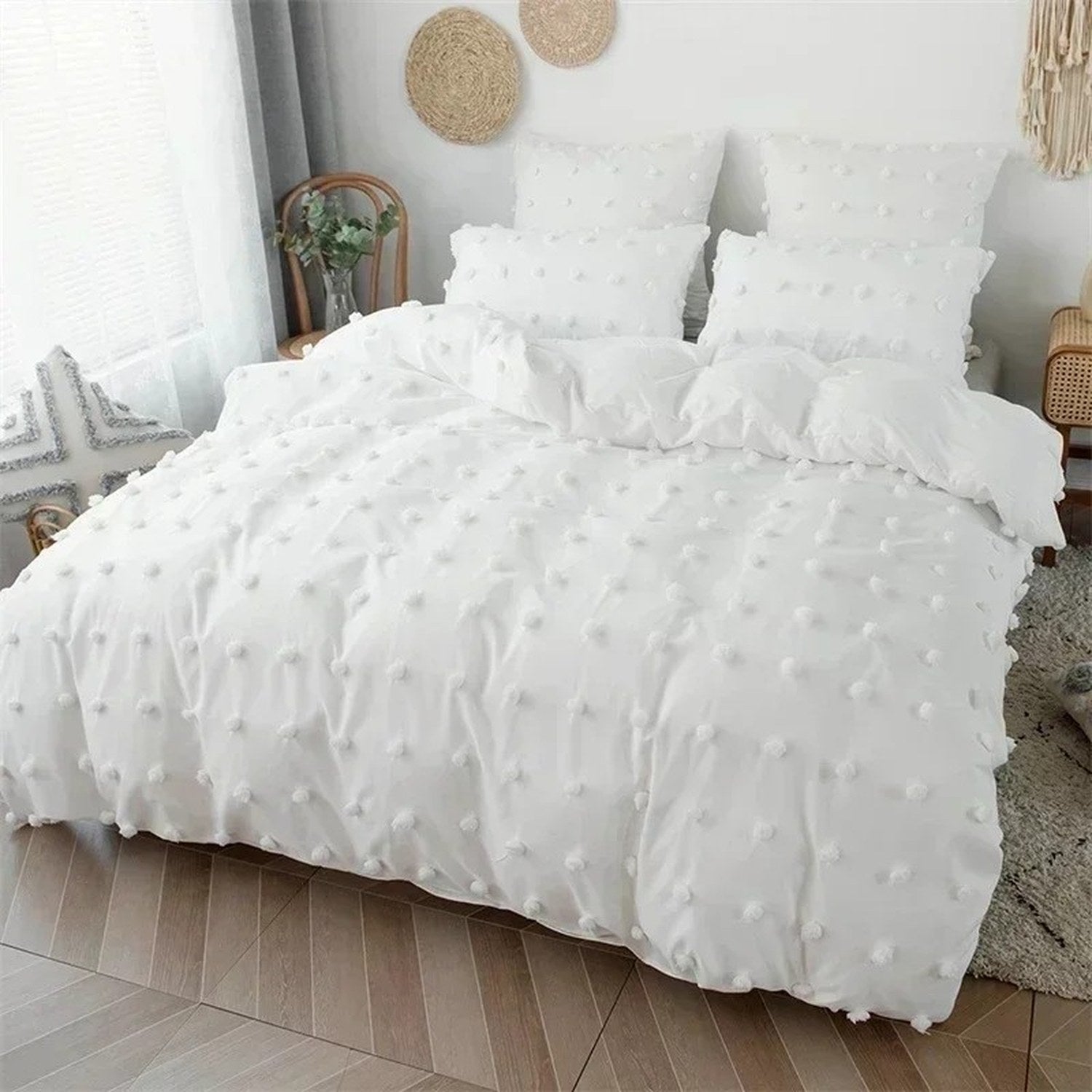 Parure de lit blanche à pompons vue de profil dans une chambre lumineuse avec chaise en rotin