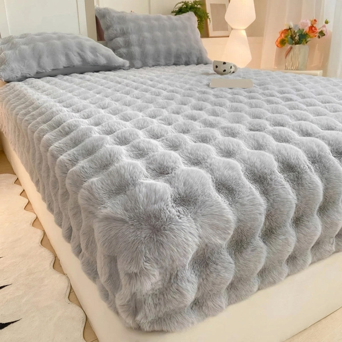 Drap-housse en peluche polaire grise sur un lit avec coussins assortis