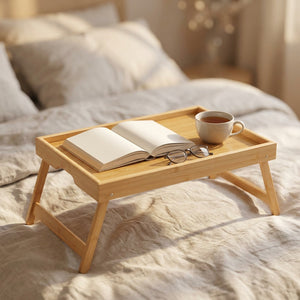 Plateau de lit en bambou avec un livre ouvert une tasse de thé et des lunettes sur un lit