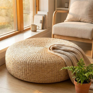 Pouf rond en paille dans un coin lecture avec plaid et plante près d'une fenêtre