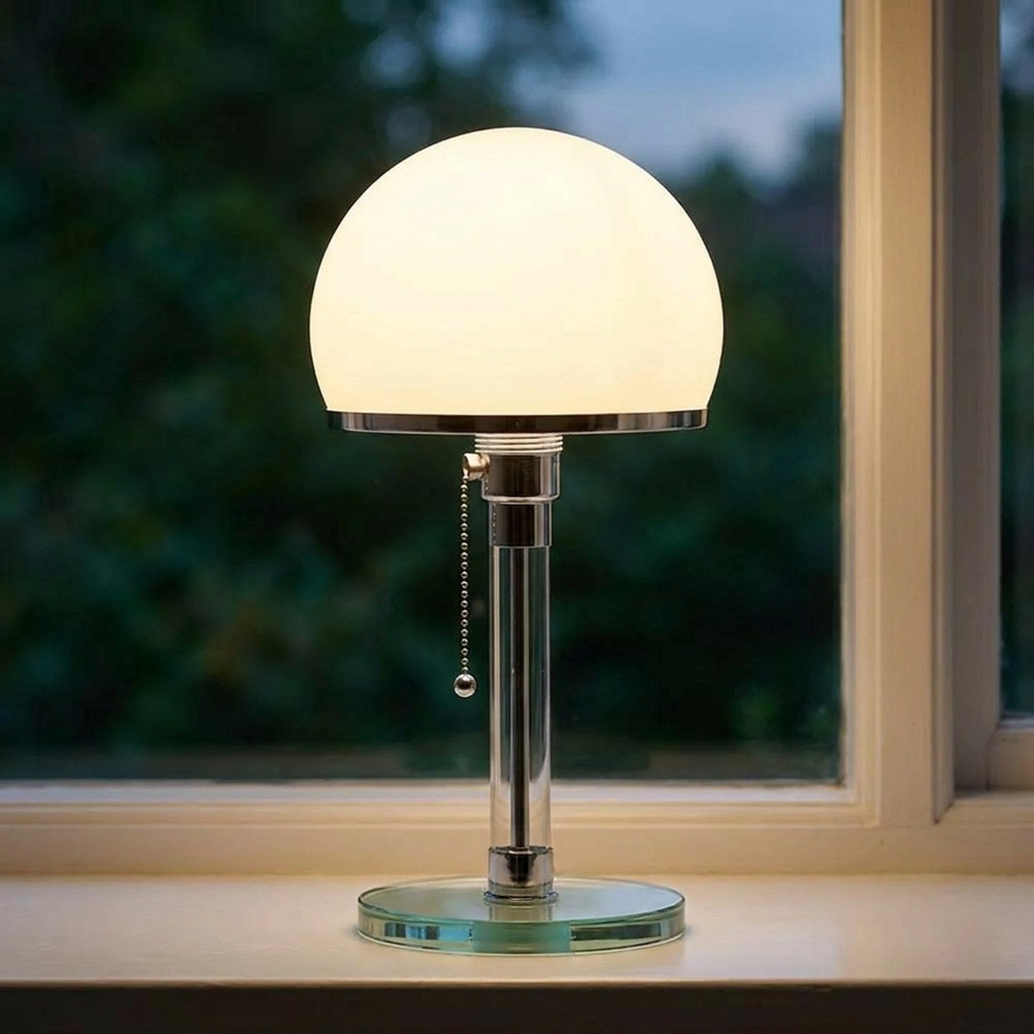 Lampe de table en verre dépoli avec pied chromé et globe lumineux allumé sur un rebord de fenêtre