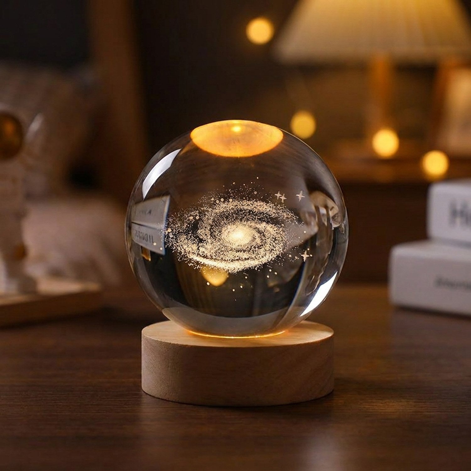 Boule de cristal gravée en 3D représentant une galaxie éclairée d'une lumière chaude sur socle en bois