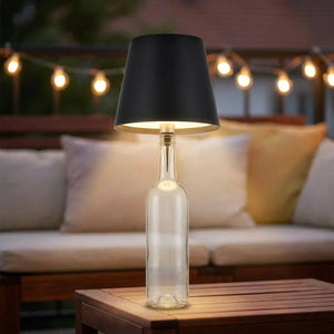 Lampe de table sans fil noire sur une bouteille sur une table de terrasse éclairée de guirlandes