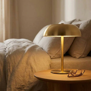 Lampe de chevet champignon dorée allumée près d'un lit dans une chambre chaleureuse
