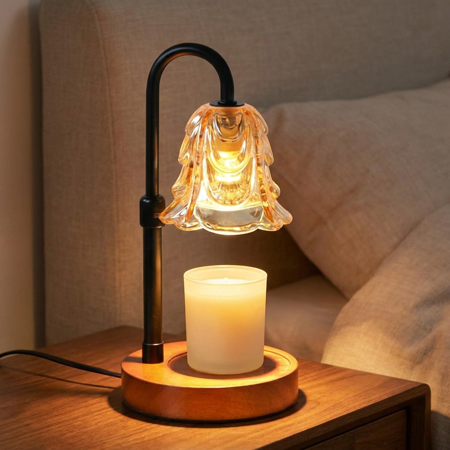 Lampe chauffe-bougie à abat-jour fleur en verre ambré allumée sur une base en bois éclairant une bougie