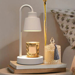 Lampe chauffe-bougie blanche posée sur une table de chevet avec bougie parfumée dorée