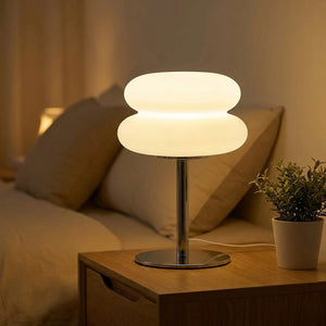 Lampe de chevet galet blanche allumée sur une table de nuit dans une chambre chaleureuse