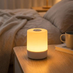 Lampe de chevet blanche cylindrique allumée avec une lumière chaude posée sur une table de nuit